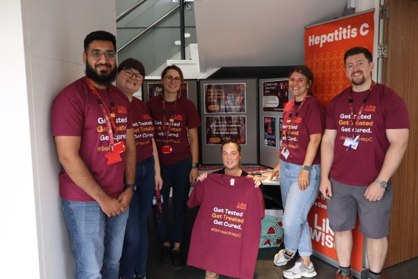 Six Likewise staff stand together wearing t-shirts that say get tested for hep c and in front of a stall all about Hep C eliminaton.