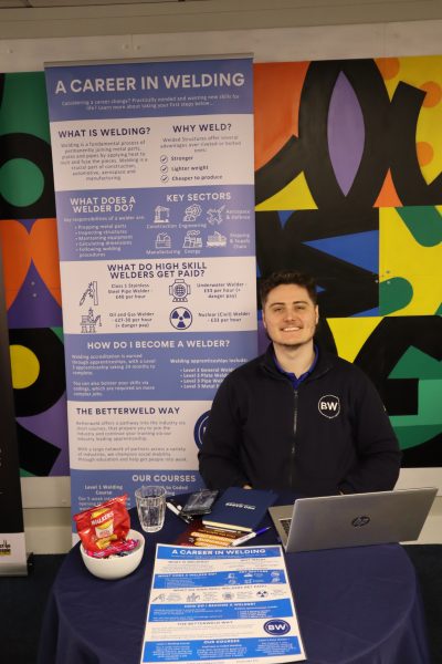 A man sits in front of a sign talking about welding