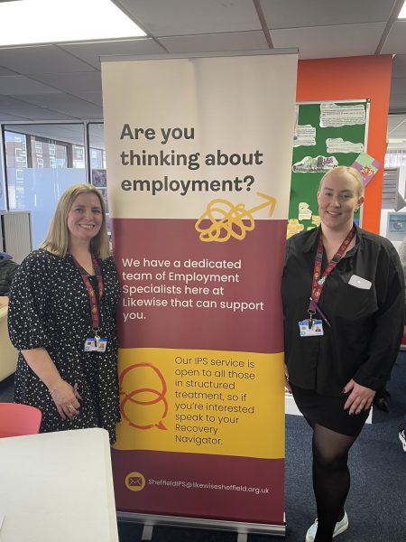 Two Likewise staff stand in front of a banner that reads are you thinking about employment