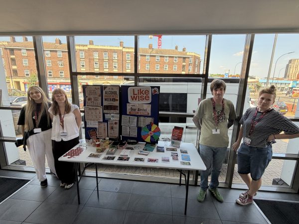 Team photo of four likewise staff standing in front of alcohol stall in reception